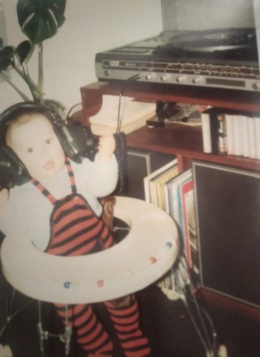 Jason as a baby in a striped romper, wearing big headphones beside a hi-fi and a shelf of records